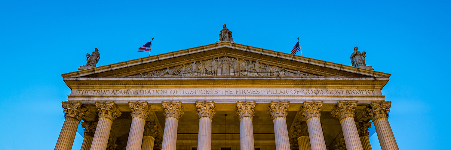 Portion of a marble Roman style courthouse against a blue sky.