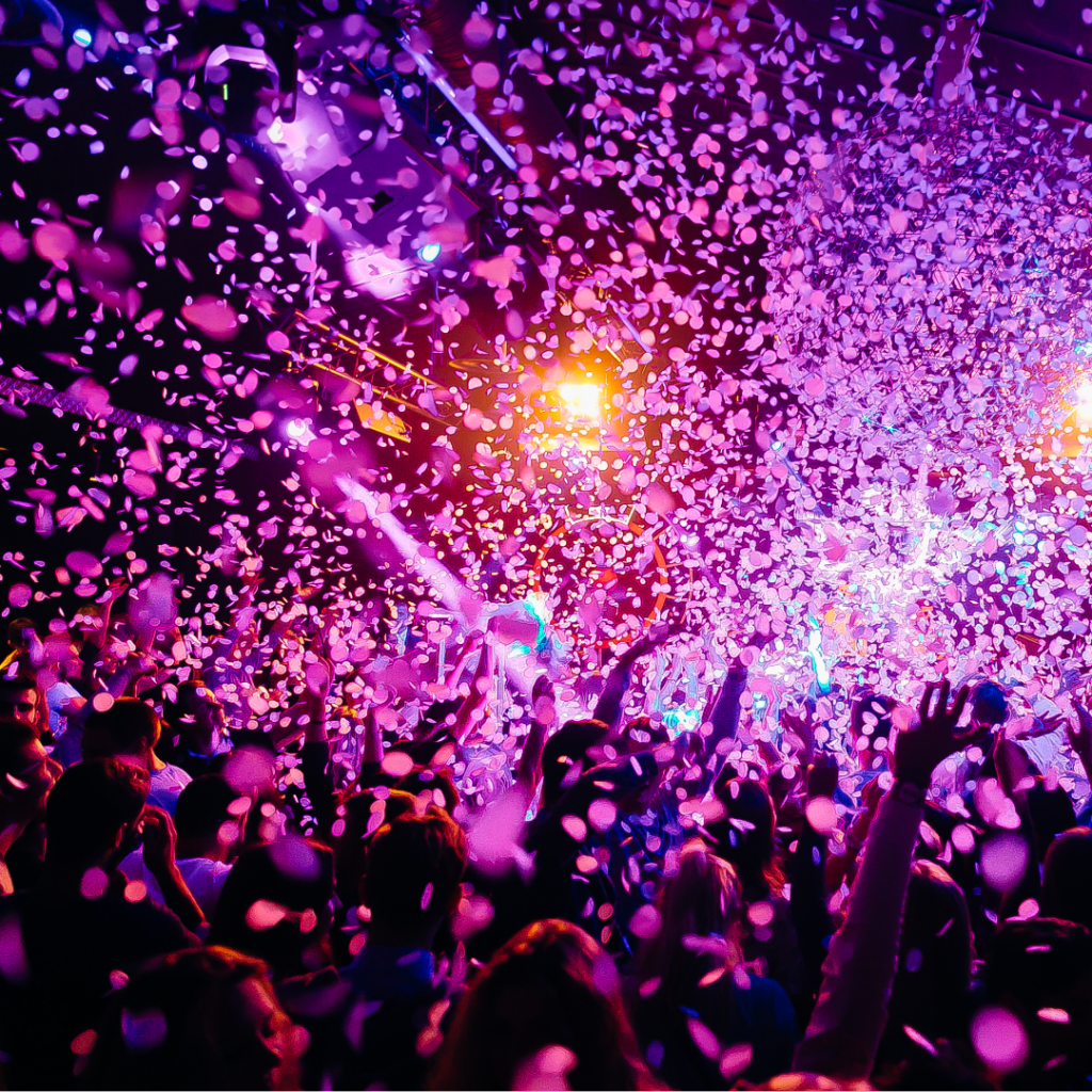 Photograph of a crowd celebrating at night with purple confetti in the air.