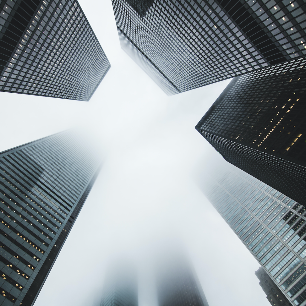 Photograph from below of several modern buildings with tops shrouded in fog.