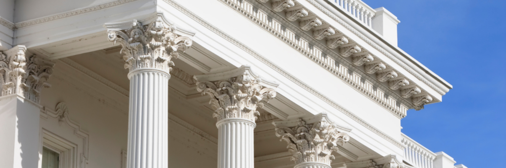 Photograph of part of a marble courthouse showing the tops of several corinthian columns.