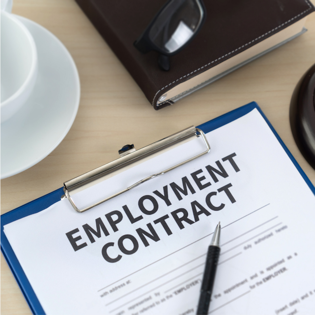 A photograph of a document entitled "Employment Contract" on top of a table with a coffee cup, a leather book and eyeglasses.