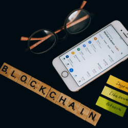 Blockchain, Crypto & NFT Photograph of a smartphone showing stock market information, eyeglasses and "Blockchain" written in letters from a Scrabble game.