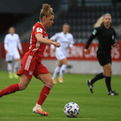 Sports Industry & Athletes Female soccer player dressed in red, about to kick a multicolored soccer ball, watched by referee and other players.